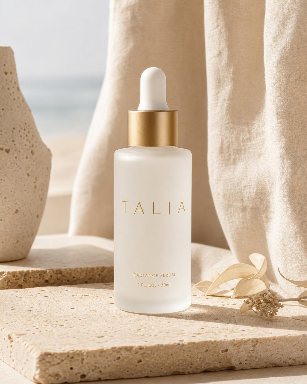 Composizione editoriale TALIA Cosmetics: flacone satinato, ramo d'ulivo e drappo su travertino